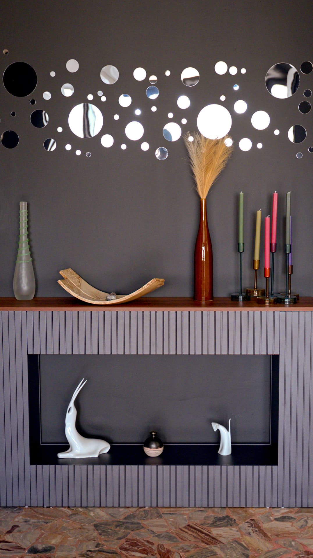 Parete con specchi circolari, candele colorate e piccole sculture