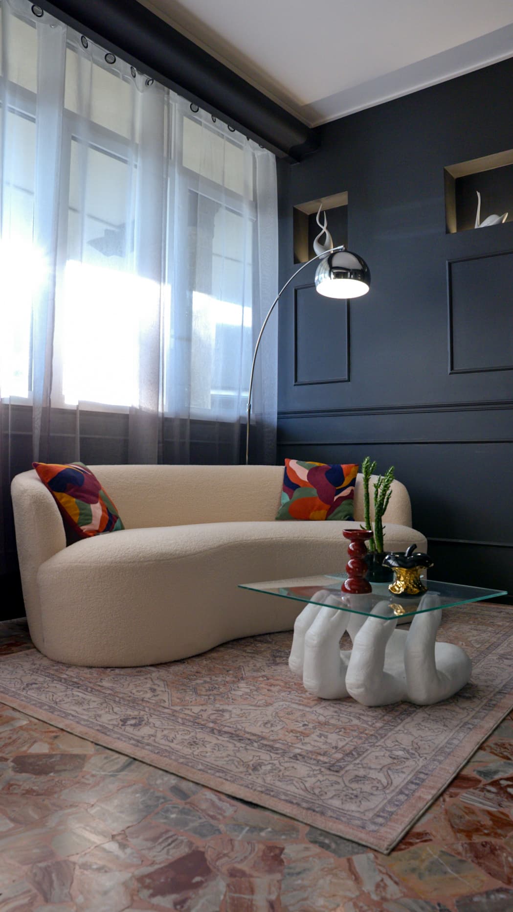 Sala d’attesa con divano curvo in bouclé, lampada ad arco e tavolino scultoreo in vetro